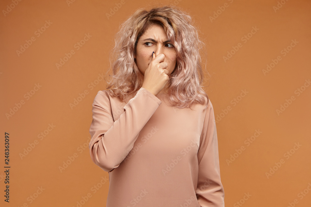 Picture of emotional displeased young European woman pinching her nose because of bad smell or gross stink. Stylish teenage girl can't stand dirty socks odour, holding breath. Body language Picture of emotional displeased young European woman pinching her nose because of bad smell or gross stink. Stylish teenage girl can't stand dirty socks odour, holding breath. Body language