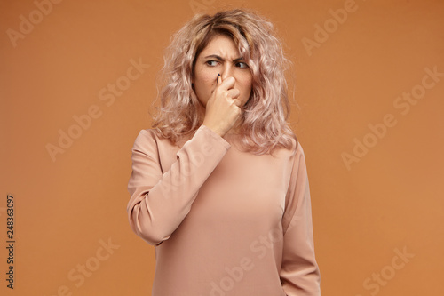Picture of emotional displeased young European woman pinching her nose because of bad smell or gross stink. Stylish teenage girl can't stand dirty socks odour, holding breath. Body language
