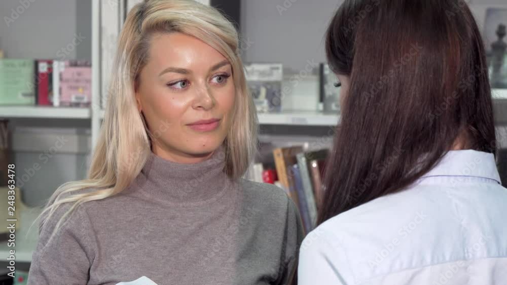 Beautiful woman smiling, talking to her friend at the bookstore or library. Gorgeous female enjoying talking to a friend at book shop. Friendship, education, consumerism concept