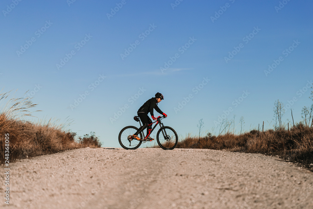 Fototapeta premium Cyclist Riding the Bike Down Rocky Hill at Sunset. Extreme Sport Concept.