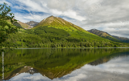Grass covered hills reflected in an alpine lake in Alaska, USA. Late afternoon light.