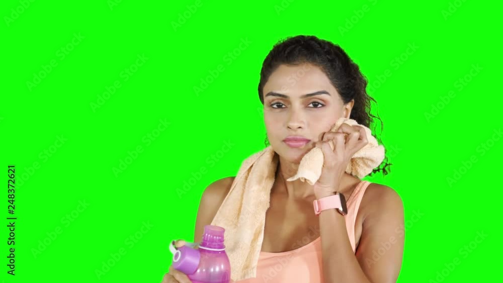 Attractive fitness woman drinking water from a bottle while wiping her sweat with a towel and smiling at the camera. Shot in 4k resolution with green screen background Attractive fitness woman drinking water from a bottle while wiping her sweat with a towel and smiling at the camera. Shot in 4k resolution with green screen background