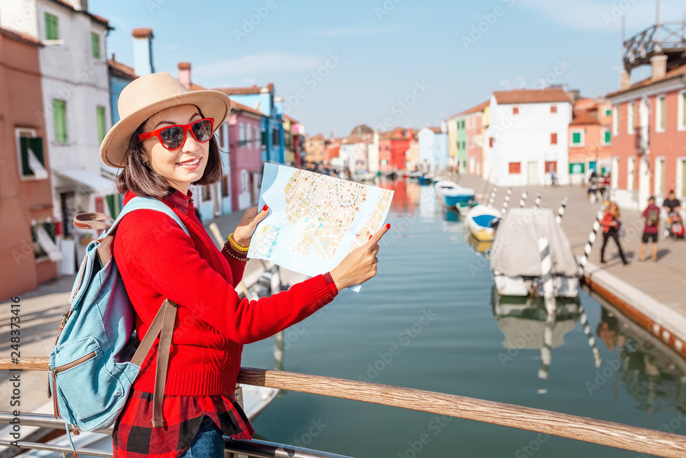 young happy traveler woman looking at the tourist map among colorful houses on Burano island, Venice. Tourism in Italy concept