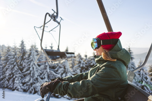 Smilling girl travels a ski lift over ski slope.