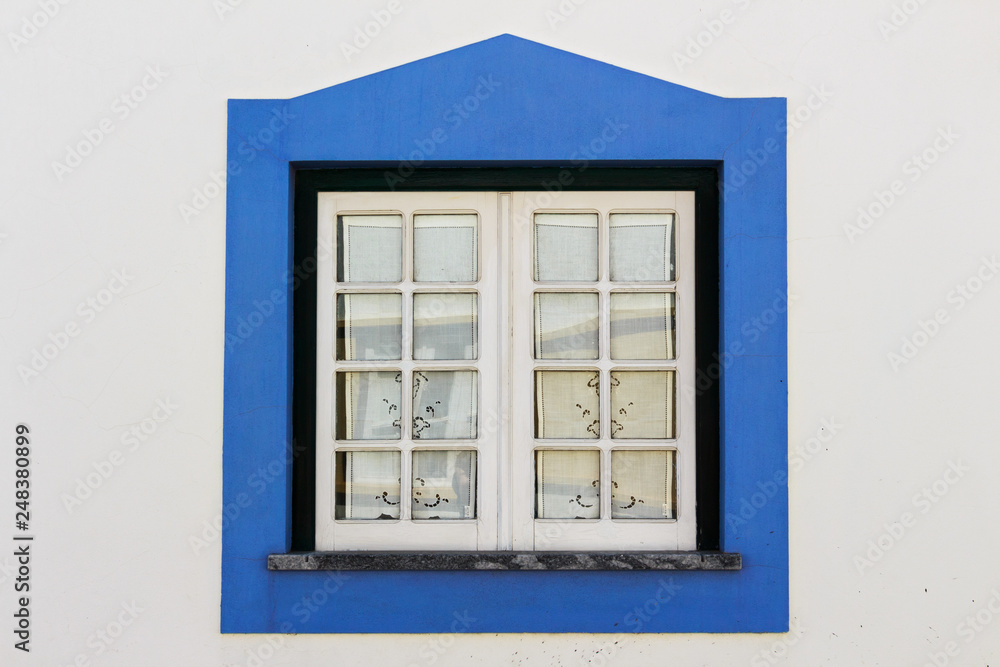 Obraz premium White wooden window with blue squared-triangular frame on white wall.