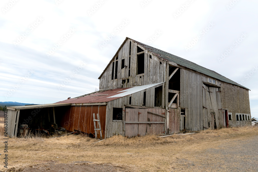 An old abandoned barn. There are holes and missing pieces in the walls. Overcast sky. An old abandoned barn. There are holes and missing pieces in the walls. Overcast sky.