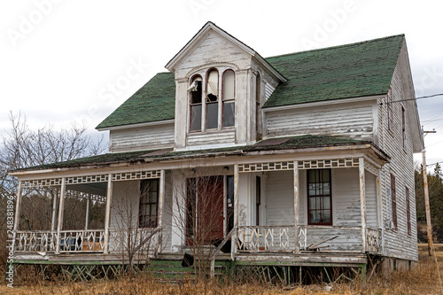 An old, abandoned house. Windows at the top are broken, the paint is peeling, and the front porch os falling down. Overcast sky. photo