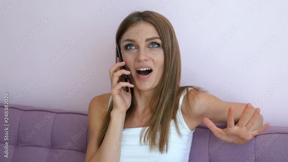 Pretty happy european woman talking on the phone while sitting on purple couch. Communication and leisure concept. Full HD