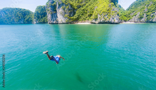 man jumping into water from a cruise boat on a sunny day in Ha Long bay, UNESCO world heritage site, Vietnam - freedom and adventure holiday concept