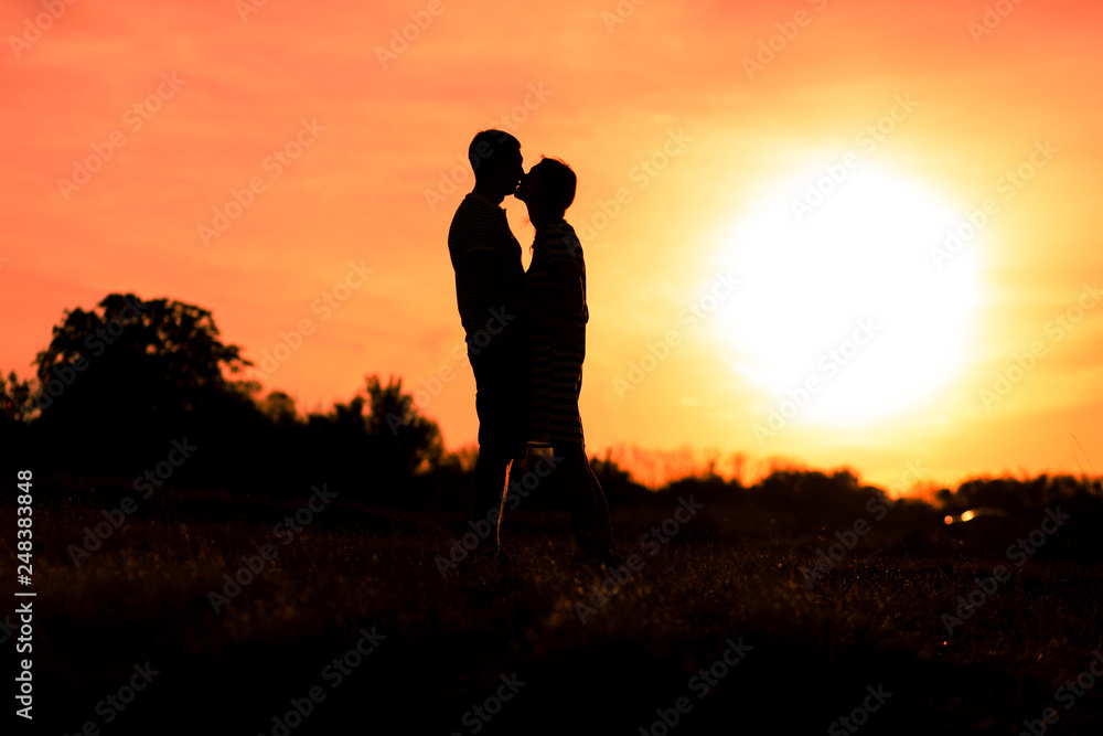 Young man and woman kissing on a romantic sunset sky background