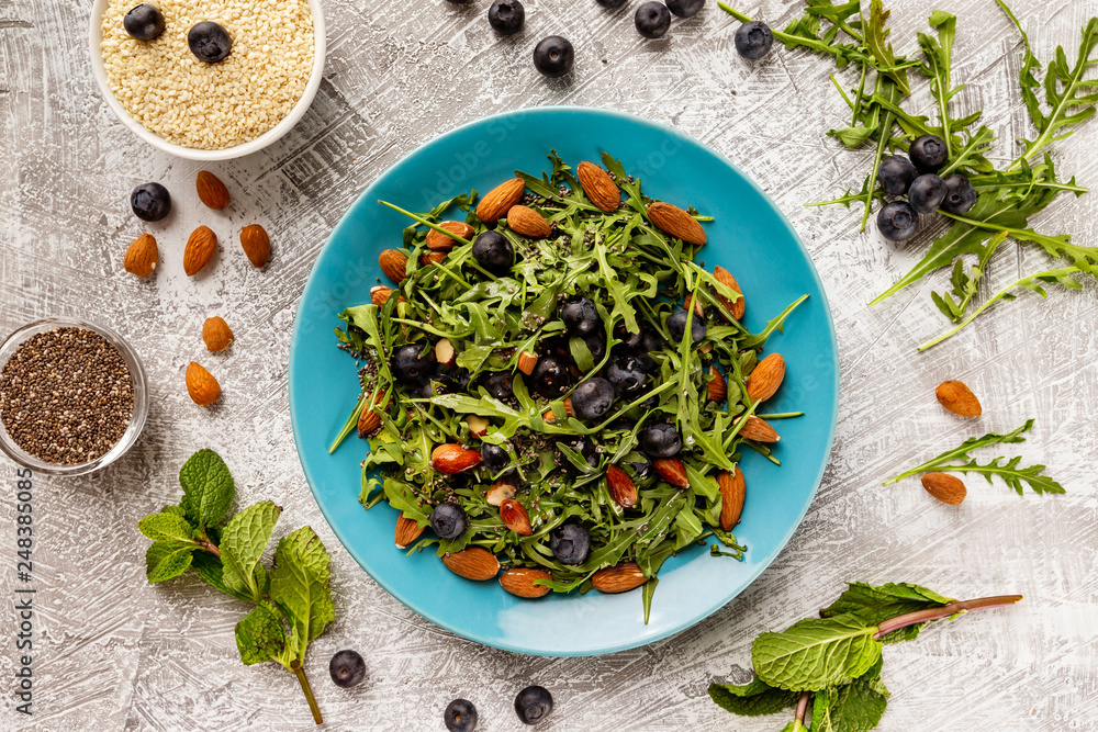 Flatlay top view plate of fresh vegetables vegetarian healthy salad with aragula, nuts, blueberry at stone table background. Flatlay top view plate of fresh vegetables vegetarian healthy salad with aragula, nuts, blueberry at stone table background.