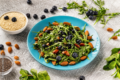 Closeup plate of fresh vegetables vegetarian healthy salad with aragula, nuts, blueberry at stone table background.