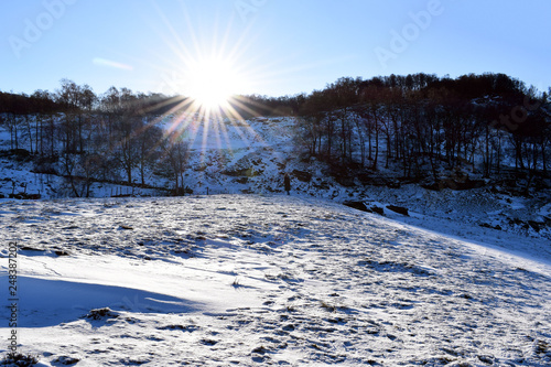 Fototapeta Naklejka Na Ścianę i Meble -  Winter landscape on a sunny day. Silhouette of a man against the background of a winter landscape. The bright sun sets over the hill on a winter day.