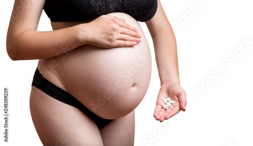 Medical theme with a pregnant woman no face in black underwear holding in her hand a bunch of white round pills close-up on a white background with copy space for text.