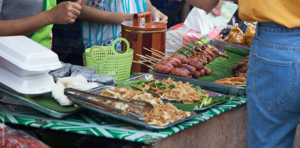 Traditional Thai food market stall selling varieties of street food, fast and comfort food such as pork or chicken skewer, pad thai, sausages. Asian Thai food industry, business and daily life concept