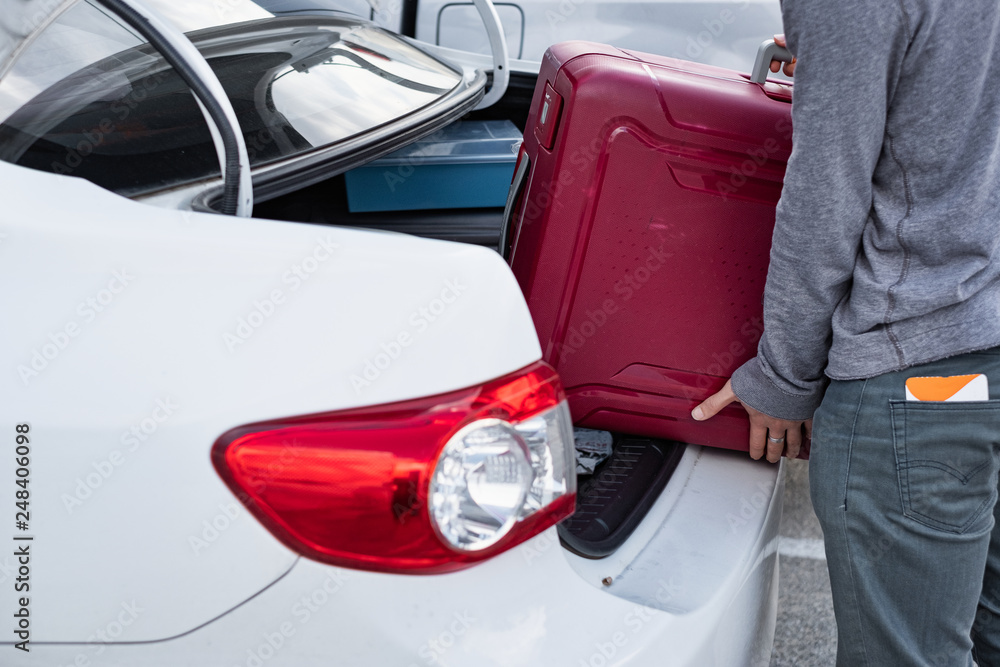 Young traveler loading and picking up red suitcase into truck of car. Young traveler loading and picking up red suitcase into truck of car.