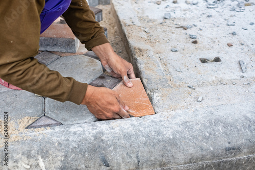 Close-up of hands of worker working on placing stone block for foot path. © phoderstock