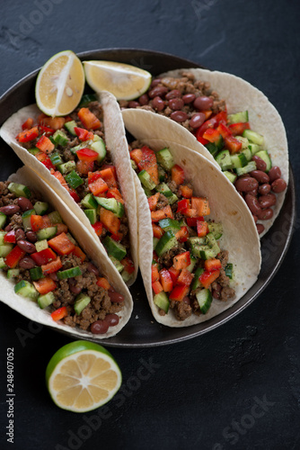 Mexican tacos with minced beef meat, red beans and fresh vegetables filling, vertical shot on a black stone surface