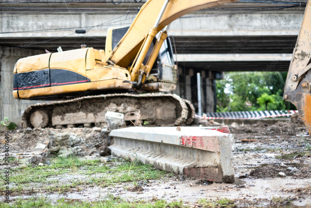 Fototapeta premium Stack of lectric poles placing in front of blue backhoe in construction site.