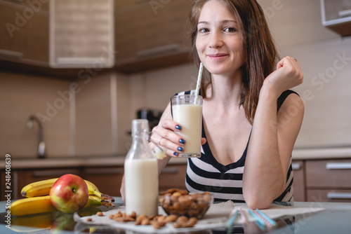 Woman drinking organic almond milk holding a glass in her hand in the kitchen. Healthy vegetarian product