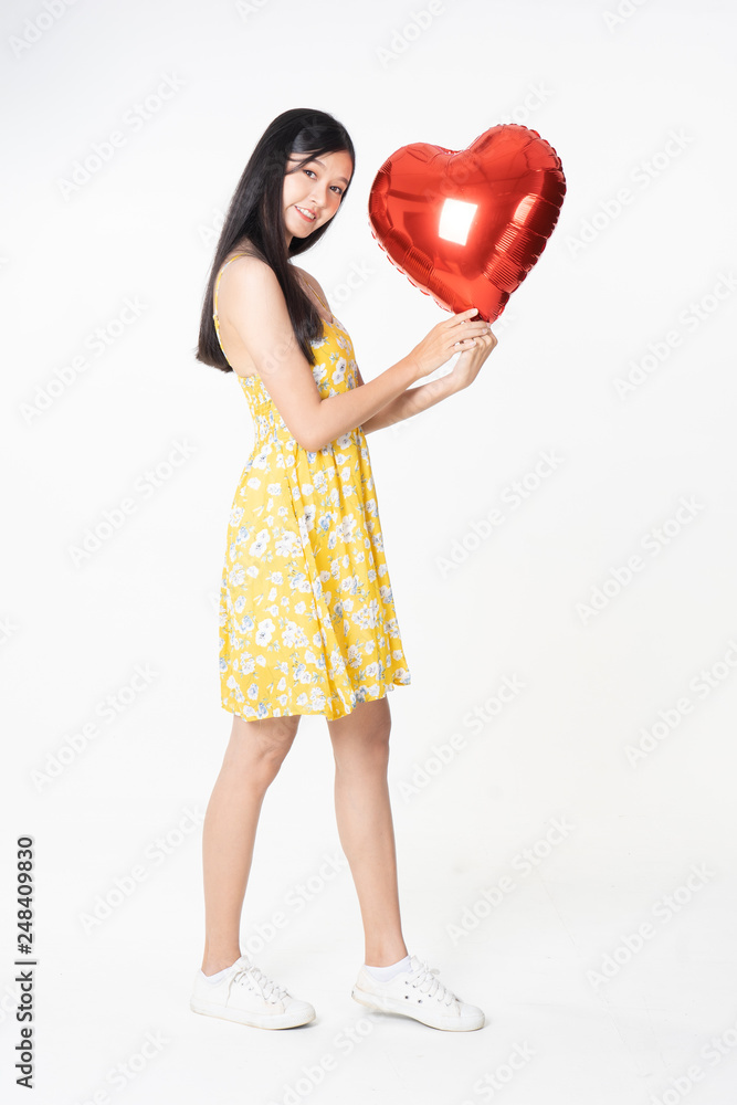 Asian young woman in yellow dress hold red balloon heart. Young woman holding it with being excited and surprised holiday present isolated white background.concept love surprise valentine day. Asian young woman in yellow dress hold red balloon heart. Young woman holding it with being excited and surprised holiday present isolated white background.concept love surprise valentine day.