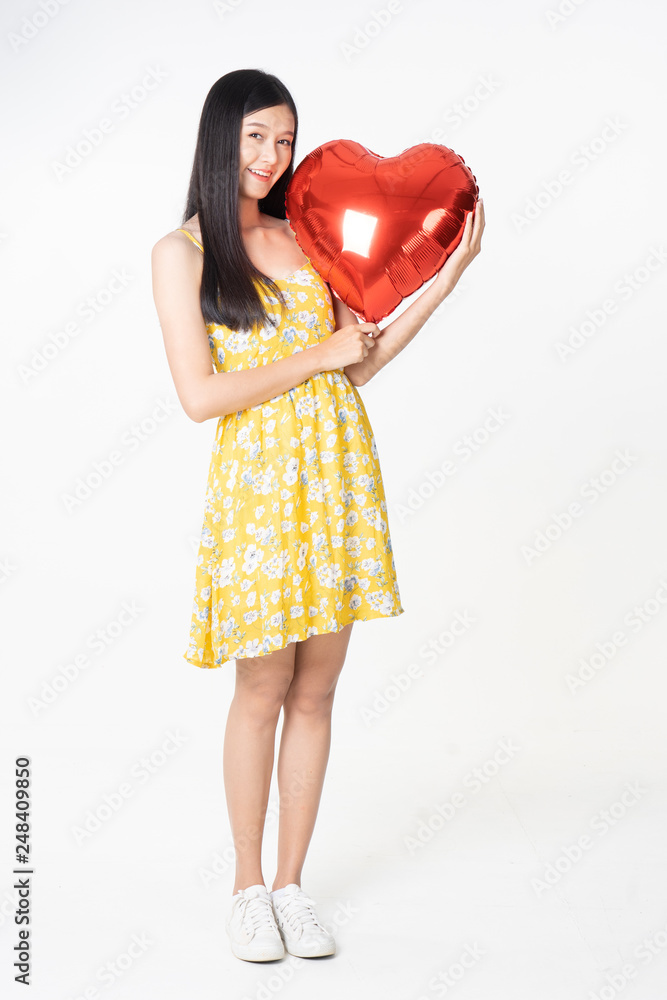 Asian young woman in yellow dress hold red balloon heart. Young woman holding it with being excited and surprised holiday present isolated white background.concept love surprise valentine day. Asian young woman in yellow dress hold red balloon heart. Young woman holding it with being excited and surprised holiday present isolated white background.concept love surprise valentine day.