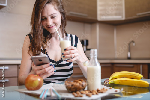 Woman drinking organic almond milk holding a phone in her hand in the kitchen. Diet healthy vegetarian product © Artem