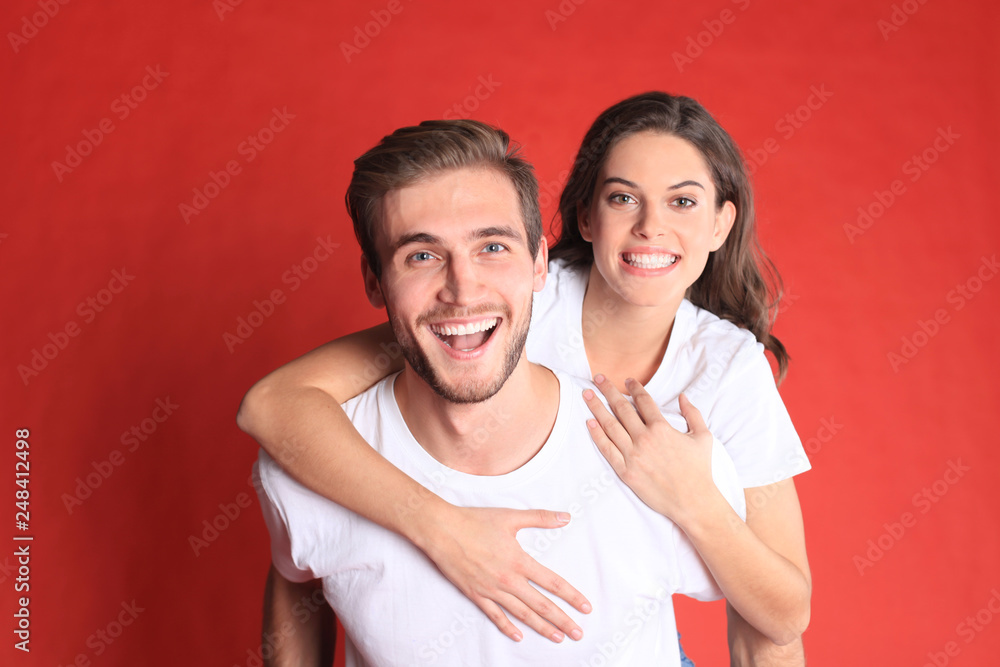 Lovely couple smiling together while sitting on back of content man over red background. Lovely couple smiling together while sitting on back of content man over red background.