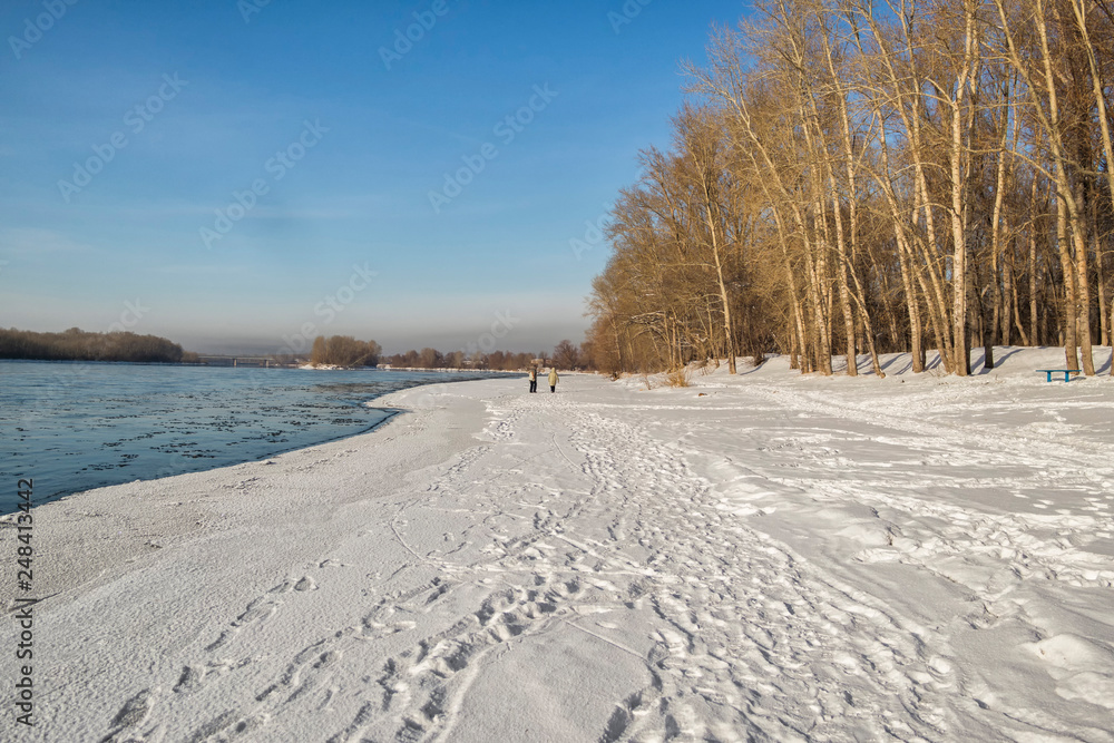 Winter landscape with the river and forest in frosty day. Irtysh river. People walk along the river. Ust-Kamenogorsk (Kazakhstan)