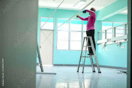 Construction worker standing on aluminium stairs or ladder using a measuring tape.