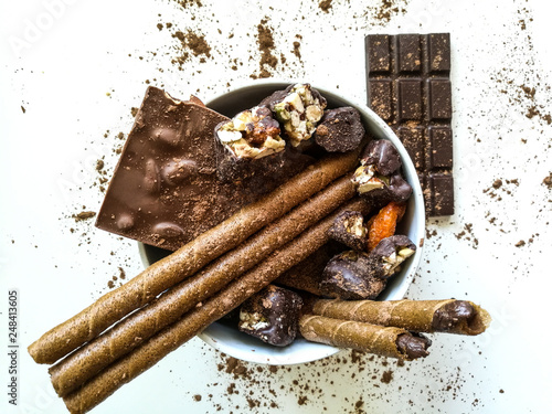 Chocolate bars, chocolates, chocolate tubes sprinkled with cocoa in a white bowl with.