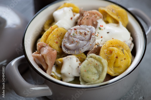Close-up of a pot with boiled colored dumplings pelmeni and sour cream, studio shot