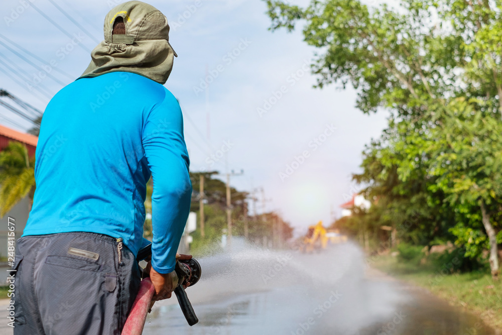 a worker spraying water to clean the road with pressurized water system, wet cleaning of street. with sun light