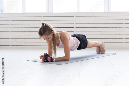 Sport, yoga and people concept - a young woman is doing a plank, taking a balance