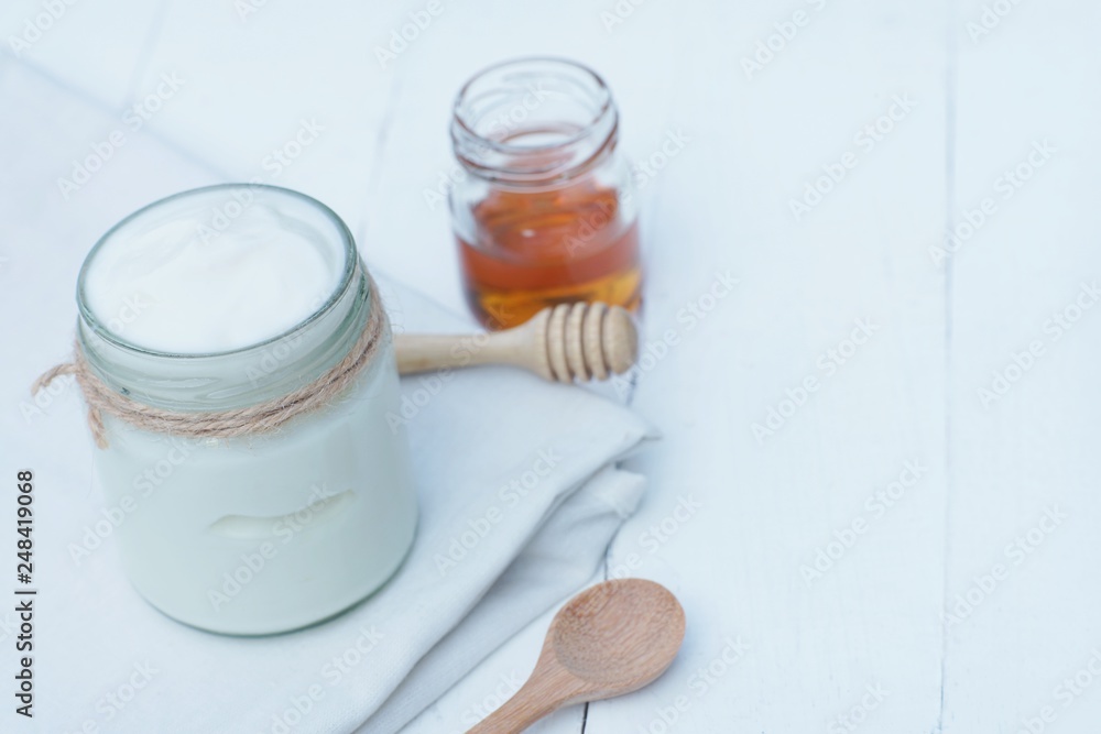 Plain yoghurt in white bowl, honey, cereal, raisin and wood spoon on white wooden table background Plain yoghurt in white bowl, honey, cereal, raisin and wood spoon on white wooden table background