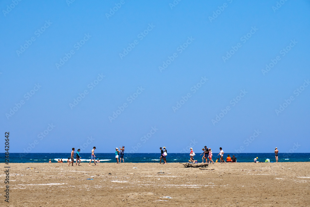 People relaxing on a sandy beach. Lots of people walking along the sandy beach of the sea