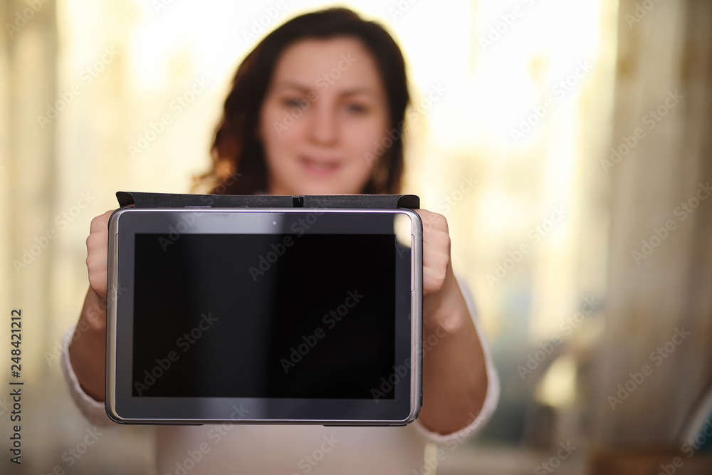 Fototapeta premium The girl is holding a tablet. The girl has a computer with a screen in her hands. Hands hold the display with an empty space.