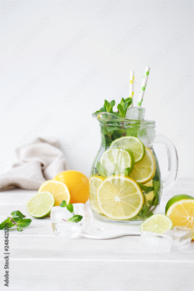 Fototapeta premium Lemonade in a glass jug on light background. Lemon, Mint, Lime and Ice Ingredients