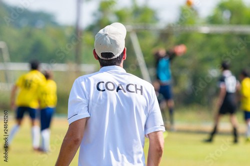 Back of football coach wearing white COACH shirt at an outdoor sport field coaching his team during a game © kudosstudio