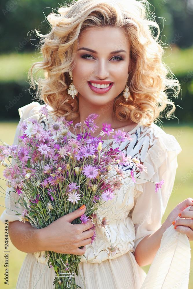 Curly blonde in a park with a bouquet of field violet flowers.. Curly blonde in a park with a bouquet of field violet flowers..
