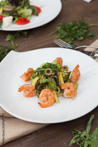 Salad with shrimps on a white plate is on the table.