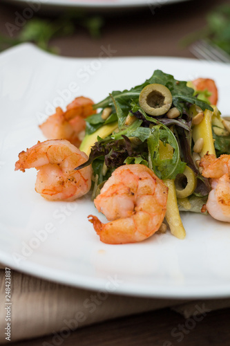 Salad with shrimps on a white plate is on the table.