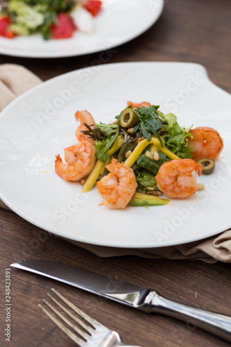 Salad with shrimps and greens on a white plate is on the table.