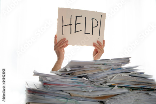 Person under a pile of papers with a hand holding a sign of help. Accounting.  photo