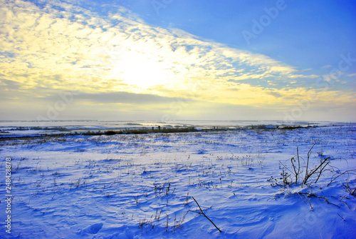 Hills covered with snow  line of houses on the hills on horizon  winter landscape  bright blue-golden cloudy evening sky with sun