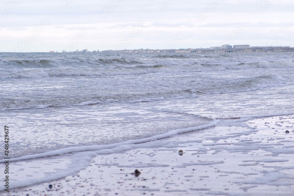 Stormy waves with foam in the sea. Sand beach in winter. Stormy waves with foam in the sea. Sand beach in winter.