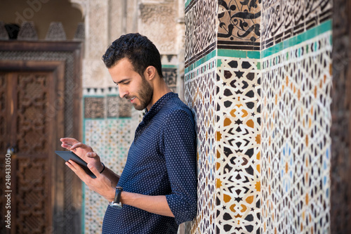 фотографія Young Muslim man in casual clothing smiling and working on tablet in traditional
