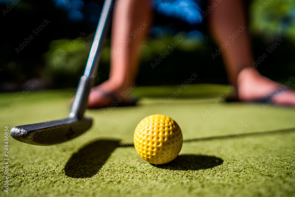 Fototapeta premium Mini Golf yellow ball with a bat near the hole at sunset