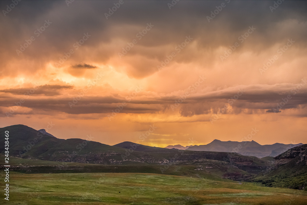 Storm clouds lit up in dramatic colours at sunset over the Drakensberg mountains surrounding the Amphitheatre, seen from Golden Gate Highlands National Park in KwaZulu Natal, South Africa