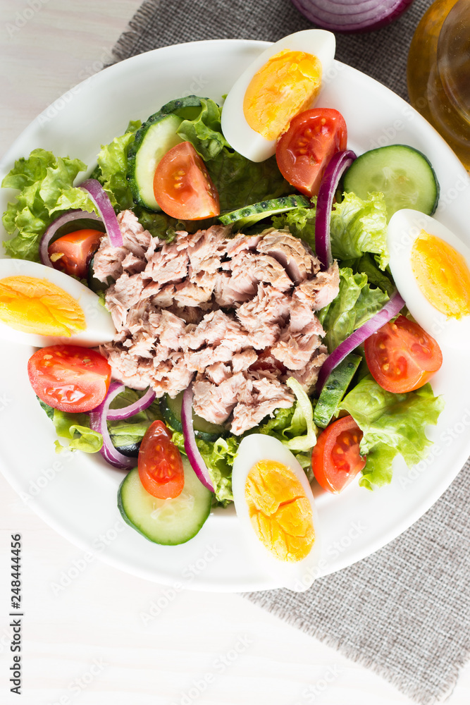 Fresh fish tuna salad made of tomato, ruccola, tuna, eggs, arugula, crackers and spices. Caesar salad in a white bowl on wooden background Fresh fish tuna salad made of tomato, ruccola, tuna, eggs, arugula, crackers and spices. Caesar salad in a white bowl on wooden background